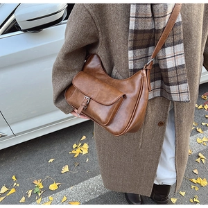 Macro detail of dark brown crescent shoulder bag with silver buckle in autumn setting
