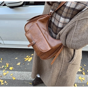 Detail of vintage brown leather hobo bag with front pocket shown in an autumn street setting