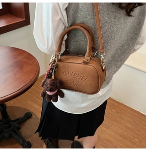 Detail of brown Boston bag with MAUDAI embossing and a cute plush bear charm