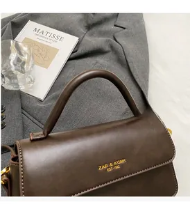 Macro shot of dark brown handbag flap with golden hardware and embossed brand lettering