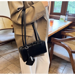 Detail of glossy black shoulder bag with a mini pouch accessory on a beige blazer
