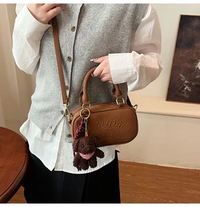 Close-up of brown bowling bag featuring embossed text and a cute teddy bear charm accessory