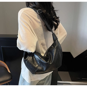 Detail of black pleated half-moon bag featuring a wide strap with silver buckle detail