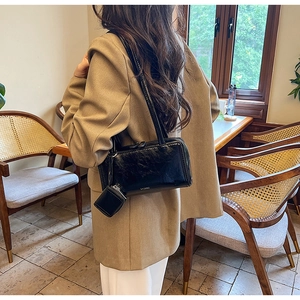 Detail of black wrinkled patent leather Boston bag with mini pouch shown in a cafe
