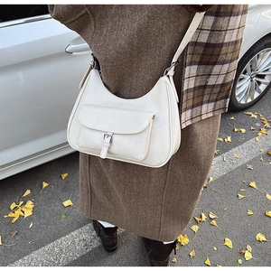 Close-up of cream-white half-moon hobo bag with front pocket shown on an autumn street