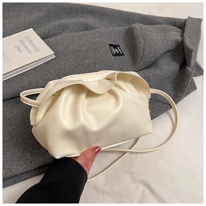 Détail d'un sac nuage plissé beige tenu sur un fond de manteau en laine élégant