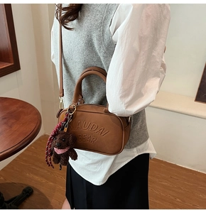 Detail of brown leather Boston bag with plush bear charm and crossbody strap