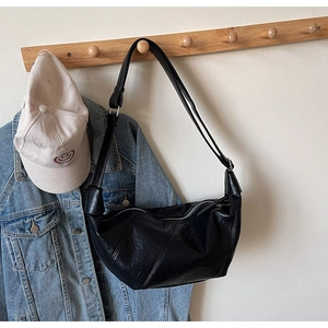 Detail of black crescent shoulder bag with glossy pleated leather texture on a wooden hanger