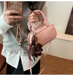 Detail of pink barrel handbag with embossed text and brown plush bear charm
