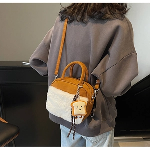 Detail of a brown suede crossbody bag with white faux fur and a cute toast pendant