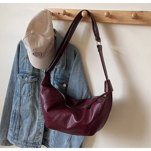 Close-up of a burgundy crescent bag with lychee texture hanging on a wooden hook