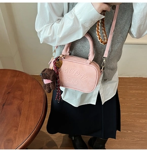 Pink matte leather crossbody bag featuring NAUDAI BEAR embossing and plush charm