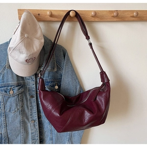 Detail of wine red crescent bag made of textured faux leather on a wooden coat hook