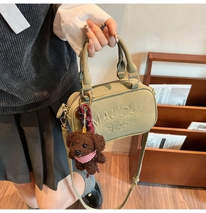 Close-up of olive green square handbag with MAUDAI BEAR embossing and cute plush dog charm
