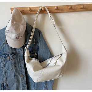Detailed close-up of cream crescent bag with litchi leather texture on wood hanger