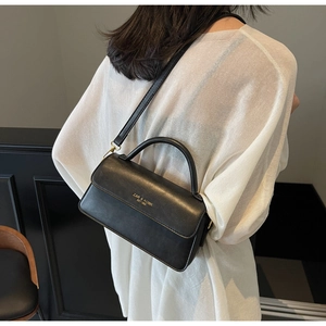 Detail of black matte leather shoulder bag featuring gold hardware and stamped brand logo
