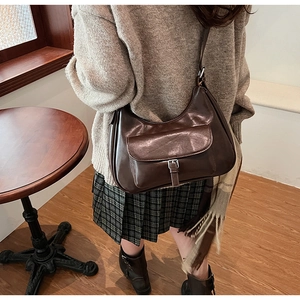 Detail of dark brown glossy leather crossbody bag with vintage buckle on a model