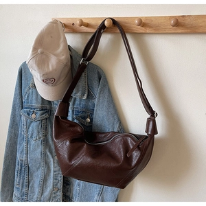 Close-up of a dark brown crescent bag hanging on a hook with casual outfit styling