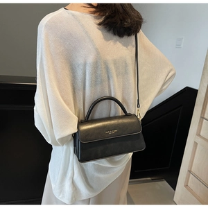 Detail of a black leather crossbody bag with top handle and gold brand logo