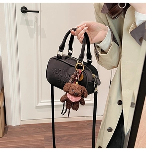 Detail of black glossy handbag with embossed letters and cute brown teddy bear charm