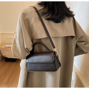 Detail of dark brown leather handbag with gold logo held by model in beige trench coat