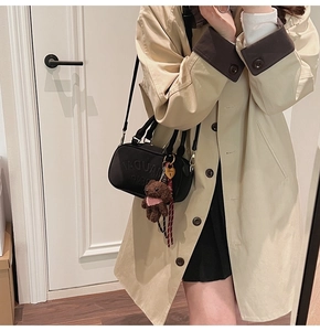 Detail of black crossbody bag with teddy bear charm and gold heart lock on trench coat