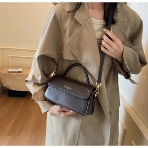 Detail of a dark brown matte leather crossbody bag with golden logo on a khaki coat