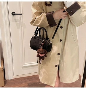 Close-up of black canvas Boston bag with embossed logo and teddy bear charm on trench coat