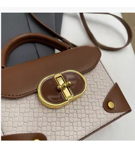 Detail of contrast stitching, woven fabric, and oval gold-tone buckle on a crossbody bag