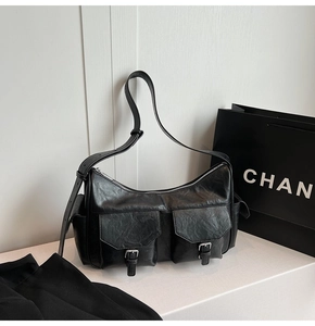 Detail of black faux leather shoulder bag featuring dual front pockets and silver buckles