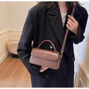 Close-up of vintage brown leather handbag with gold branding and matte metal hardware