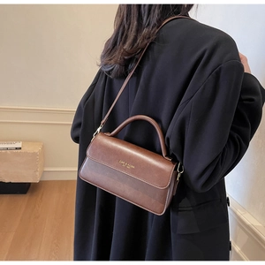 Brown vintage leather crossbody bag with top handle shown on a model in side view