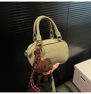 Detail of green mini boston handbag with embossed lettering and plush bear charm