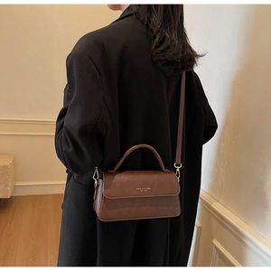 Close-up of brown leather crossbody bag showing metallic logo and premium texture