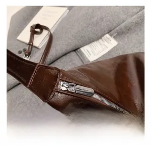 Detail view of silver metal zipper and adjustable strap on dark brown glossy leather bag