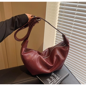 Close-up of a burgundy glossy leather crescent bag with adjustable strap in home setting