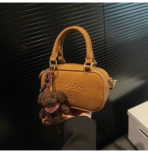 Detailed shot of brown suede handbag with embossed logo and a cute plush bear charm