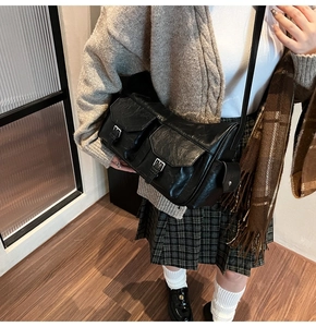 Close-up of vintage black faux leather messenger bag with dual metal buckle front pockets