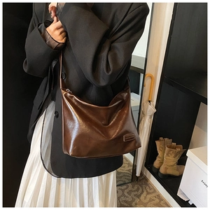 Close-up of a glossy dark brown faux leather shoulder bag worn with a chic blazer