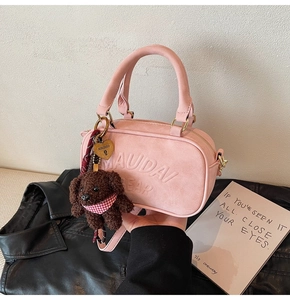 Detail of pink suede crossbody bag with teddy bear charm and gold hardware on leather jacket