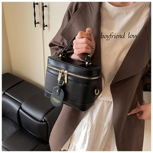 Detail shot of black box-shaped bucket bag with gold zipper and leather logo tag