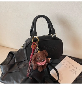 Detail of a black matte crossbody bag with embossed lettering and plush puppy charm