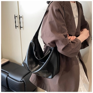 Detailed shot of a black glossy soft leather hobo bag with wide shoulder strap worn by model