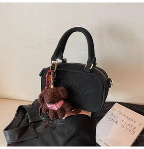 Detail of black crossbody bag with embossed AUDAI lettering and cute dog charm