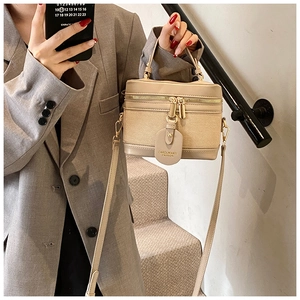 Detail view of beige box-style handbag with gold zippers and adjustable shoulder strap