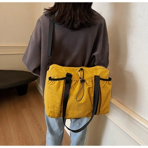 Detail of yellow nylon tote bag featuring black webbing straps and functional side pockets