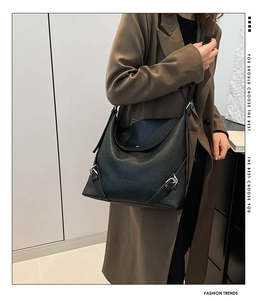 Detail of black pebbled leather tote bag with silver buckle accents worn by a model