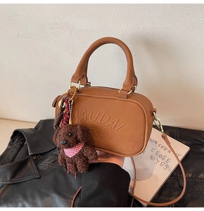 Detail of brown PU leather crossbody bag with MAUDAI BEAR embossed text and a cute puppy charm
