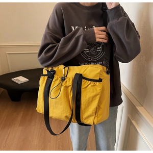 Detailed view of yellow nylon tote bag featuring black wide strap and drawstring pocket