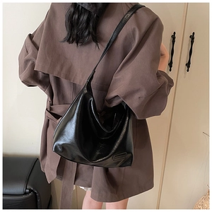 Close-up of a black glossy hobo bag worn with a brown trench coat in an indoor setting